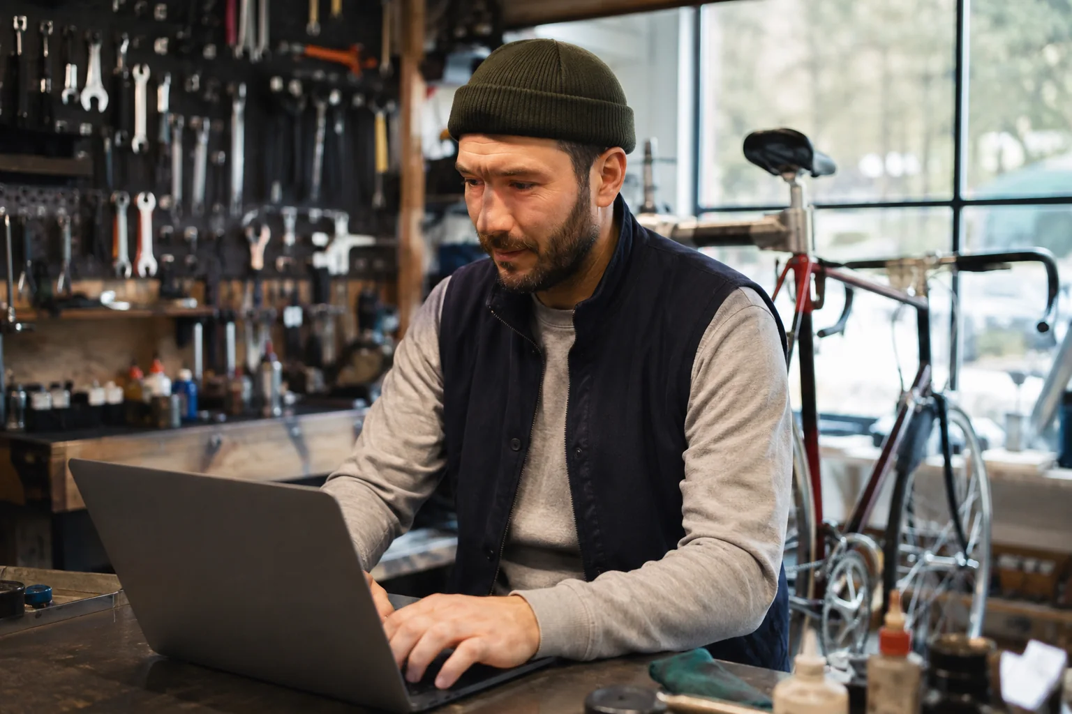 Bicycle repair shop owner working on a laptop at a workbench